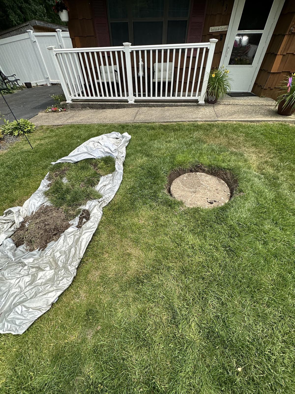 Cesspool cover uncovered in a front lawn with the sod set aside on a tarp