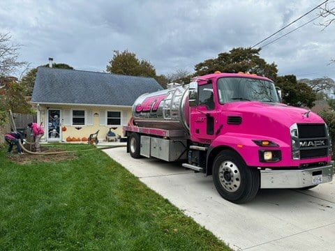JET pink pump truck in a driveway while two technicians work on a cesspool in the front yard