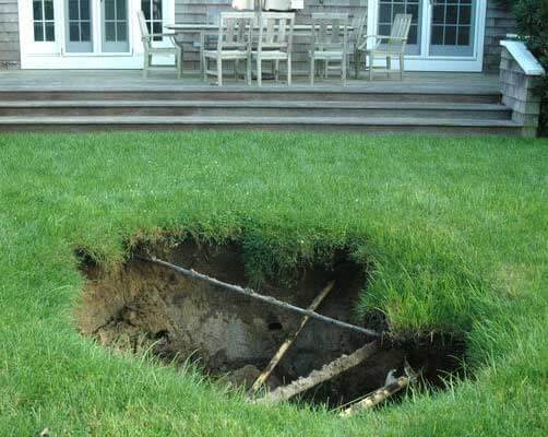 Collapsed cesspool opening in a backyard lawn